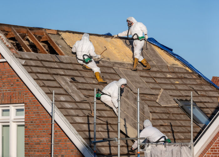 Professionals in protective suits remove asbestos-cement roofing underlayment