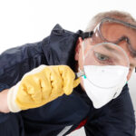 a pest control contractor or exterminator with a magnifying glass in his typical work dress at his work with chemicals against mold, pests bugs