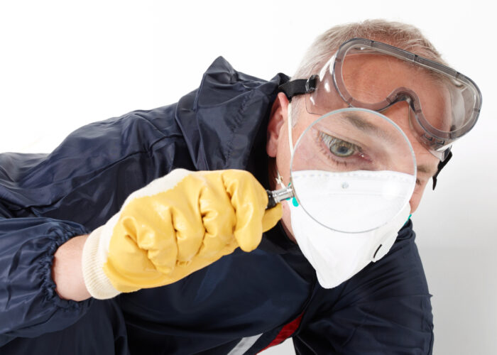 a pest control contractor or exterminator with a magnifying glass in his typical work dress at his work with chemicals against mold, pests bugs