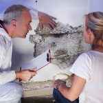 pest control contractor or exterminator with a blonde female customer at a mold destroyed wall and explain her the problem